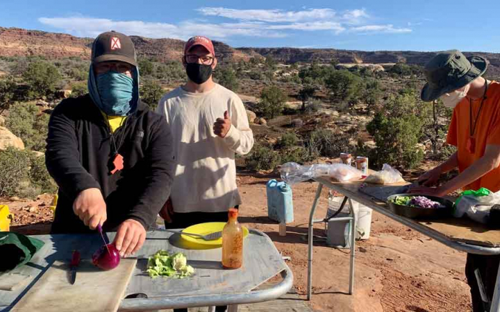 Three people prepare food on tables outdoors.